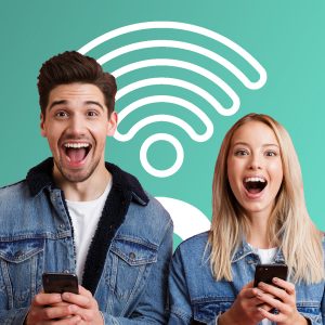 Portrait of an excited young couple dressed in denim jackets standing together isolated over red background, using mobile phones